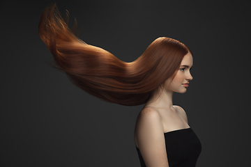 Image showing Beautiful model with long smooth, flying red hair isolated on dark studio background.