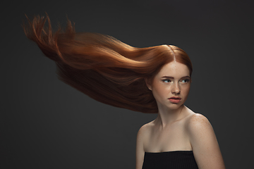 Image showing Beautiful model with long smooth, flying red hair isolated on dark studio background.