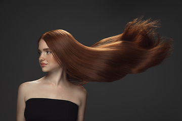 Image showing Beautiful model with long smooth, flying red hair isolated on dark studio background.