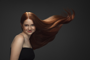 Image showing Beautiful model with long smooth, flying red hair isolated on dark studio background.