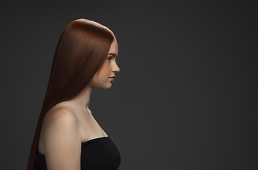 Image showing Beautiful model with long smooth, flying red hair isolated on dark studio background.