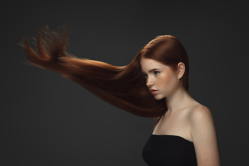 Image showing Beautiful model with long smooth, flying red hair isolated on dark studio background.