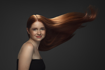 Image showing Beautiful model with long smooth, flying red hair isolated on dark studio background.