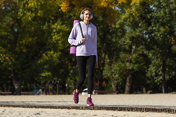 Image showing Young woman training outdoors in autumn sunshine. Concept of sport, healthy lifestyle, movement, activity.