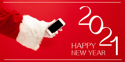 Image showing Hand of Santa Claus holding phone, greeting with New Year 2021 and Christmas. Flyer with copyspace