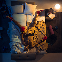 Image showing Top view of young professional boxer, fighter sleeping at his bedroom in sportwear with gloves