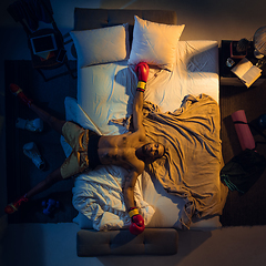 Image showing Top view of young professional boxer, fighter sleeping at his bedroom in sportwear with gloves