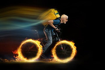 Image showing Fast delivery service - deliveryman on bicycle driving with order in fire on dark background