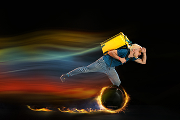 Image showing Fast delivery service - deliveryman on unicycle driving with order in fire on dark background