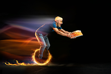 Image showing Fast delivery service - deliveryman on unicycle driving with order in fire on dark background