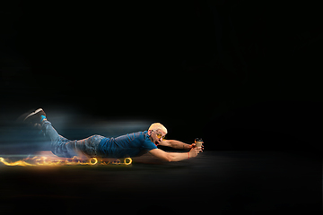 Image showing Fast delivery service - deliveryman on skateboard driving with order in fire on dark background