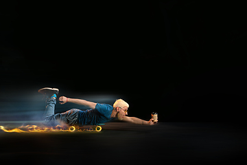 Image showing Fast delivery service - deliveryman on skateboard driving with order in fire on dark background