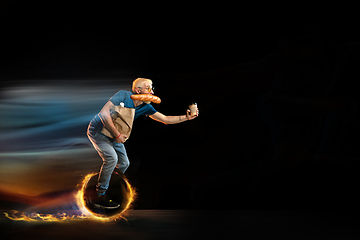 Image showing Fast delivery service - deliveryman on unicycle driving with order in fire on dark background