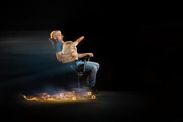 Image showing Fast delivery service - deliveryman on chair driving with order in fire on dark background