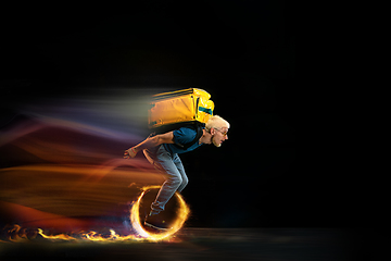 Image showing Fast delivery service - deliveryman on unicycle driving with order in fire on dark background