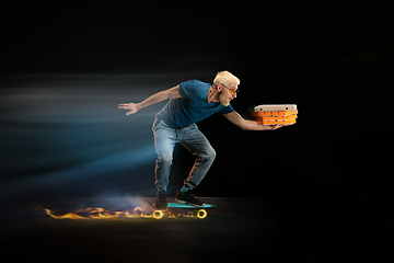 Image showing Fast delivery service - deliveryman on unicycle driving with order in fire on dark background