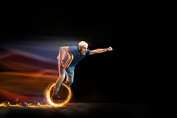 Image showing Fast delivery service - deliveryman on unicycle driving with order in fire on dark background