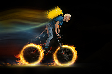 Image showing Fast delivery service - deliveryman on bicycle driving with order in fire on dark background