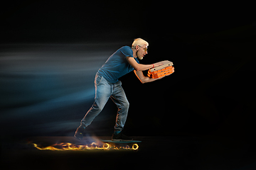 Image showing Fast delivery service - deliveryman on unicycle driving with order in fire on dark background