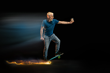 Image showing Fast delivery service - deliveryman on skateboard driving with order in fire on dark background