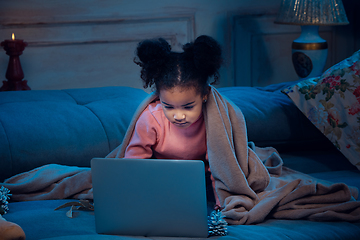 Image showing Happy african-american little girl during video call with laptop and home devices, looks delighted and happy