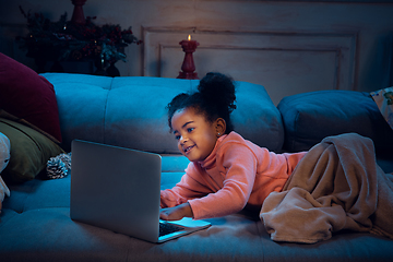 Image showing Happy african-american little girl during video call with laptop and home devices, looks delighted and happy