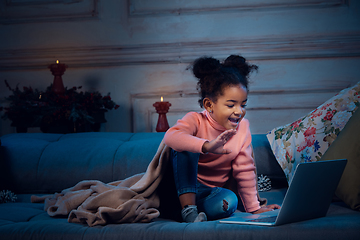 Image showing Happy african-american little girl during video call with laptop and home devices, looks delighted and happy