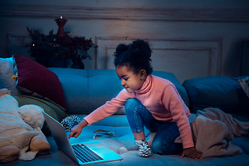 Image showing Happy african-american little girl during video call with laptop and home devices, looks delighted and happy