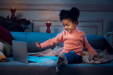 Image showing Happy african-american little girl during video call with laptop and home devices, looks delighted and happy