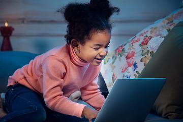 Image showing Happy african-american little girl during video call with laptop and home devices, looks delighted and happy