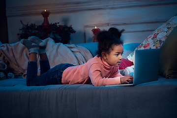 Image showing Happy african-american little girl during video call with laptop and home devices, looks delighted and happy