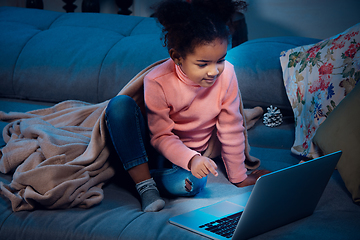 Image showing Happy african-american little girl during video call with laptop and home devices, looks delighted and happy