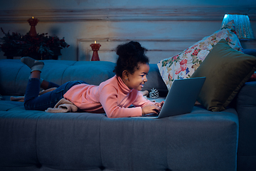 Image showing Happy african-american little girl during video call with laptop and home devices, looks delighted and happy