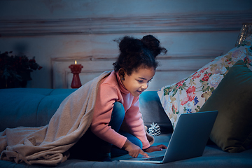 Image showing Happy african-american little girl during video call with laptop and home devices, looks delighted and happy