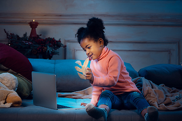 Image showing Happy african-american little girl during video call with laptop and home devices, looks delighted and happy