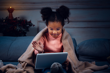 Image showing Happy african-american little girl during video call with laptop and home devices, looks delighted and happy