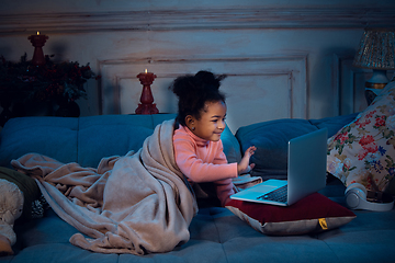 Image showing Happy african-american little girl during video call with laptop and home devices, looks delighted and happy