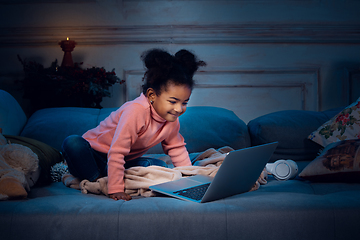 Image showing Happy african-american little girl during video call with laptop and home devices, looks delighted and happy