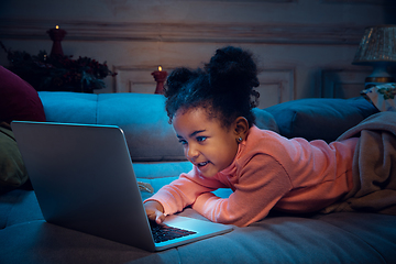 Image showing Happy african-american little girl during video call with laptop and home devices, looks delighted and happy