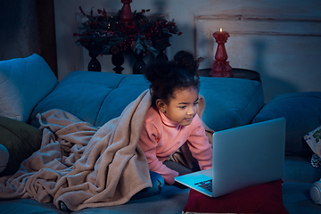 Image showing Happy african-american little girl during video call with laptop and home devices, looks delighted and happy