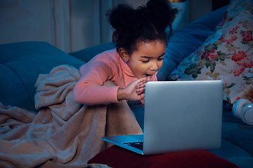 Image showing Happy african-american little girl during video call with laptop and home devices, looks delighted and happy