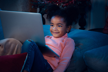 Image showing Happy african-american little girl during video call with laptop and home devices, looks delighted and happy