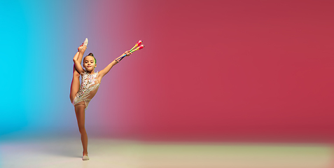 Image showing Little caucasian girl, rhytmic gymnast training, performing isolated on gradient blue-red studio background in neon