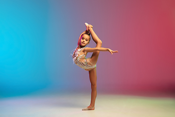 Image showing Little caucasian girl, rhytmic gymnast training, performing isolated on gradient blue-red studio background in neon