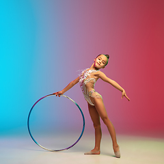 Image showing Little caucasian girl, rhytmic gymnast training, performing isolated on gradient blue-red studio background in neon