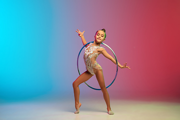 Image showing Little caucasian girl, rhytmic gymnast training, performing isolated on gradient blue-red studio background in neon