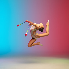 Image showing Little caucasian girl, rhytmic gymnast training, performing isolated on gradient blue-red studio background in neon