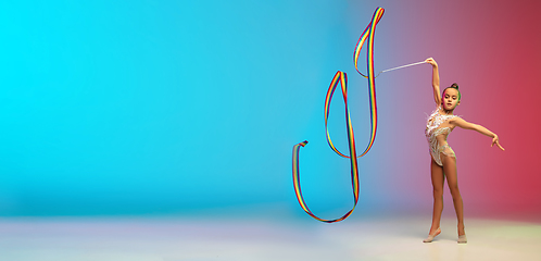 Image showing Little caucasian girl, rhytmic gymnast training, performing isolated on gradient blue-red studio background in neon