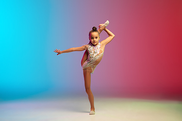 Image showing Little caucasian girl, rhytmic gymnast training, performing isolated on gradient blue-red studio background in neon