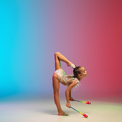 Image showing Little caucasian girl, rhytmic gymnast training, performing isolated on gradient blue-red studio background in neon